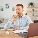 Eating the fruit. Man with banana sitting by the table with laptop on it and have fun