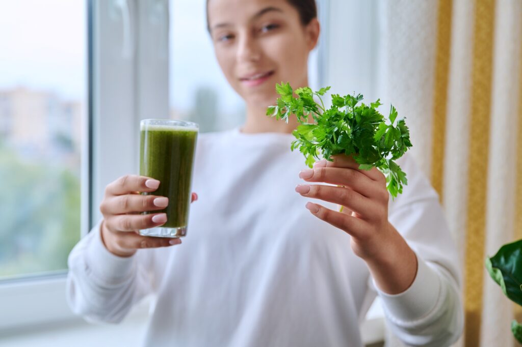 Fresh green drink with parsley vegetables fruit in hands of young female