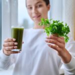 Fresh green drink with parsley vegetables fruit in hands of young female