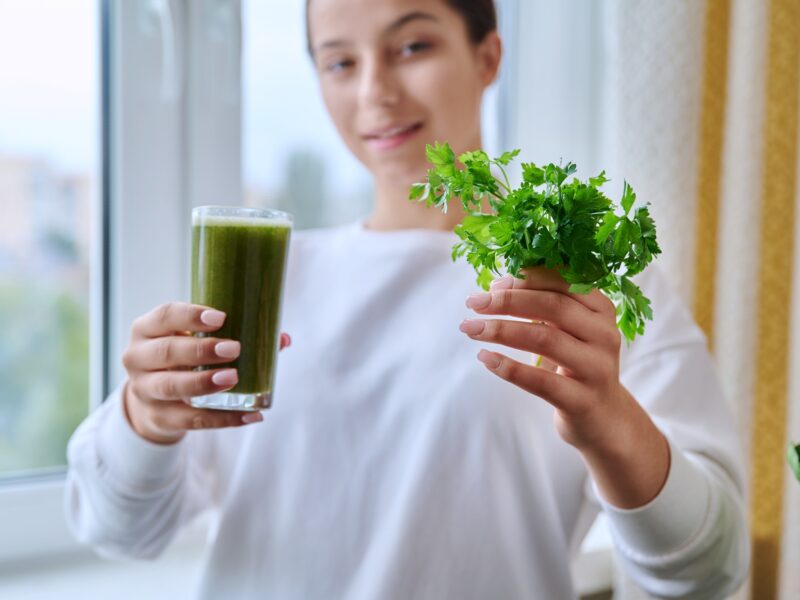 Fresh green drink with parsley vegetables fruit in hands of young female